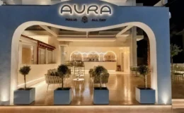 Aura All Day Bar στα Μάλια Κρήτης με καμπύλη είσοδο και φωτιζόμενη επιγραφή.