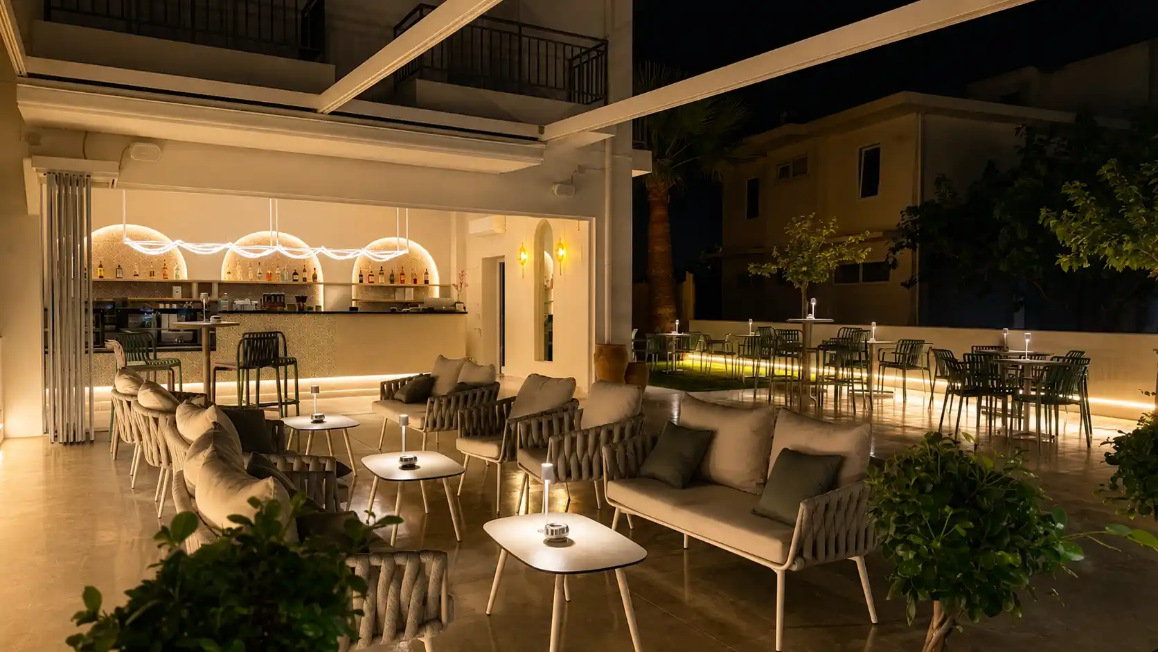 Εξωτερικός χώρος του Aura All Day Bar στα Μάλια με lounge καθιστικά, τραπεζοκαθίσματα και φωτισμένο bar