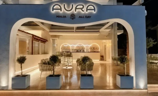Aura All Day Bar στα Μάλια Κρήτης με καμπύλη είσοδο και φωτιζόμενη επιγραφή.