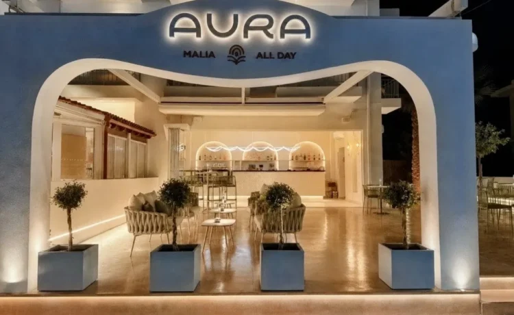 Aura All Day Bar στα Μάλια Κρήτης με καμπύλη είσοδο και φωτιζόμενη επιγραφή.