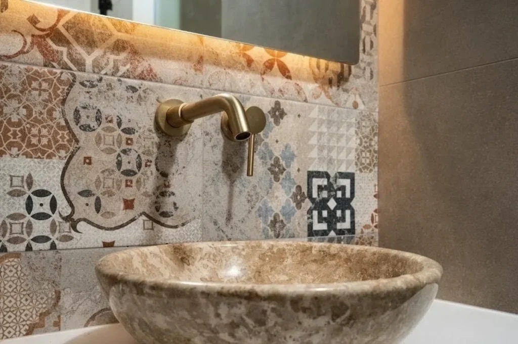 Μεσογειακό μπάνιο με patterned πλακάκια, πέτρινο νιπτήρα και ορειχάλκινη μπαταρία.